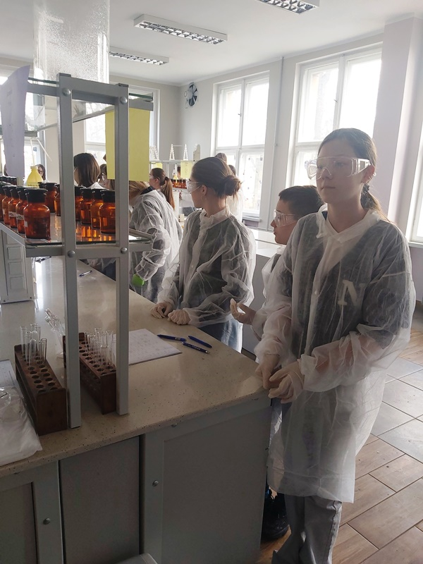 Maja, Piotr i Amelia w fartuchach laboratoryjnych i goglach czekają na zadania laboratoryjne