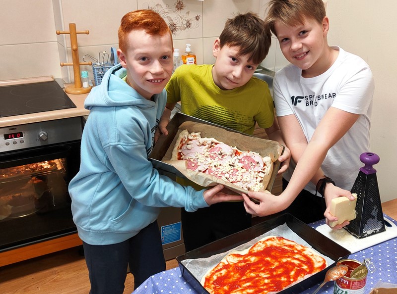Chłopcy pozują z wykonaną przez siebie pizzą, gotową do wstawienia do piekarnika
