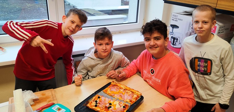 Chłopcy siedzą przy stoliku, na którym leży upieczona pizza
