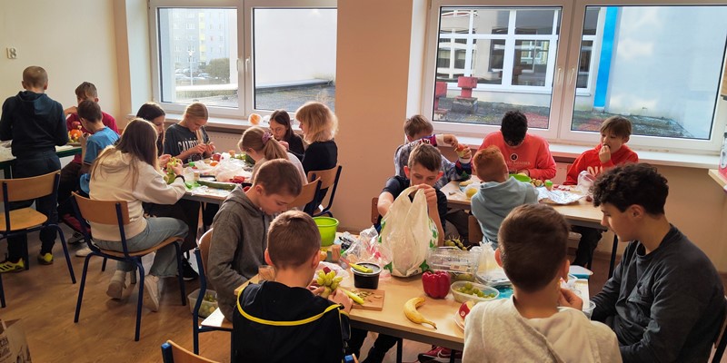 Uczniowie klasy 5a siedzą przy stolikach i wykonują warzywno-owocowe zwierzaki
