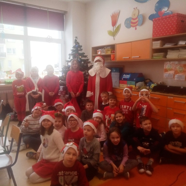 Uczniowie klasy 2c pozują w swojej klasopracowni przy choince do zdjęcia z Mikołajem oraz reniferem, część uczniów ma na głowie mikołajkowe czapki.