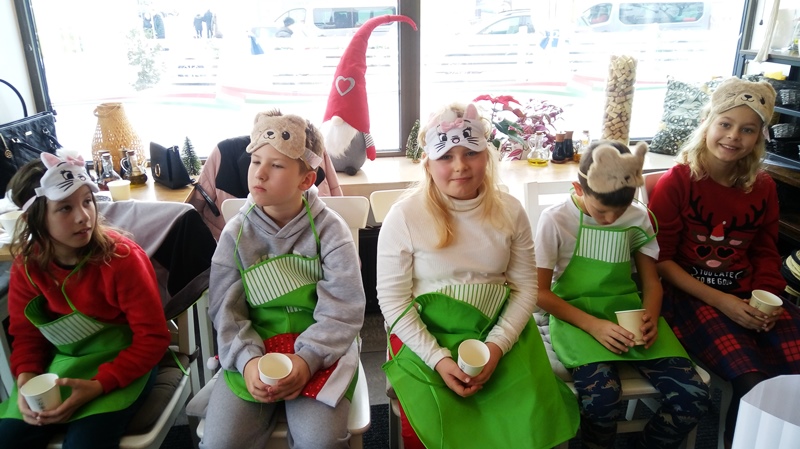 Czworo dzieci siedzi na krzesłach, trzymają kubeczki i uczestniczą w konkursie rozpoznawania smaków.