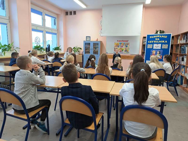 Uczniowie wraz z prowadzącą konkurs nauczycielką Małgorzatą Pyrsz słuchają recytacji dziewczynki z klasy pierwszej.