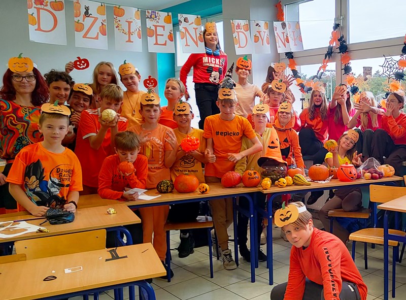Uczniowie klasy 5a ubrani na pomarańczowo z dekoracjami jesiennymi